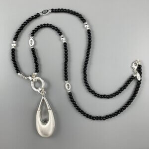 Long black bead necklace interspersed with silver beads and silver oval links, with a large solid teardrop pendant hanging from a silver ring